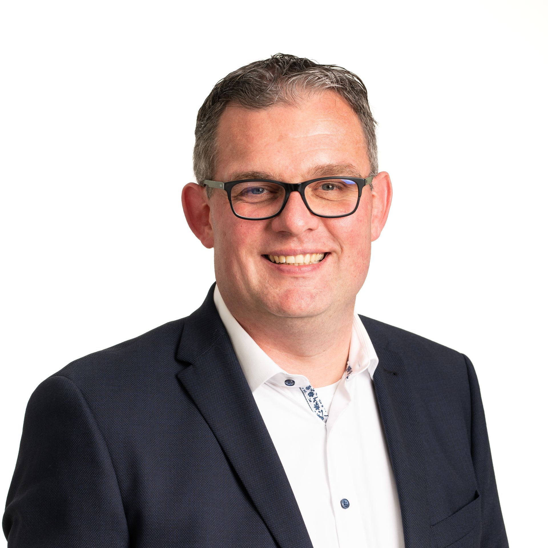 Man met bril en donkerblauwe blazer lacht naar de camera, witte achtergrond.