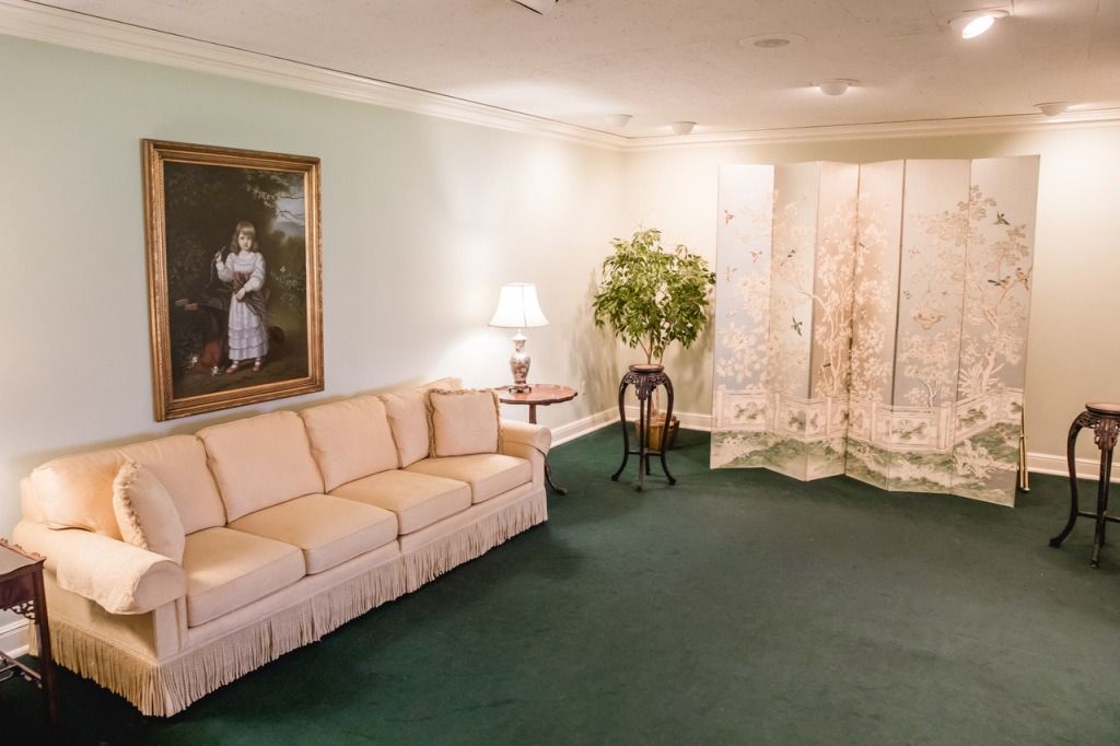 A room with a sofa, artwork, and a screen; green carpet, light walls.