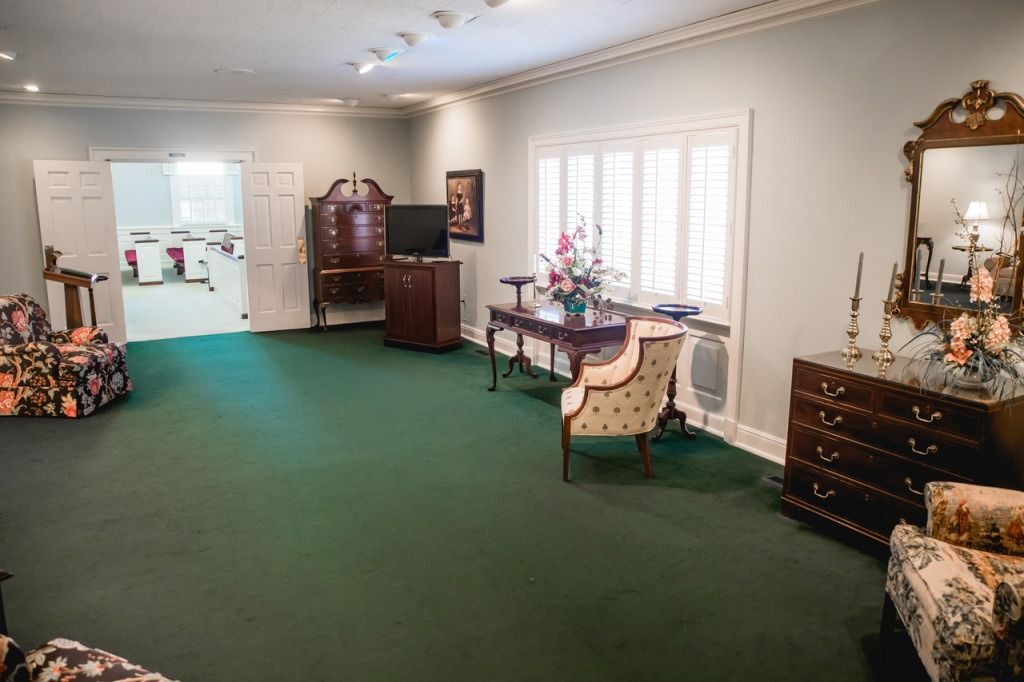 Interior of a room with green carpet, furniture, desk, and a large mirror.