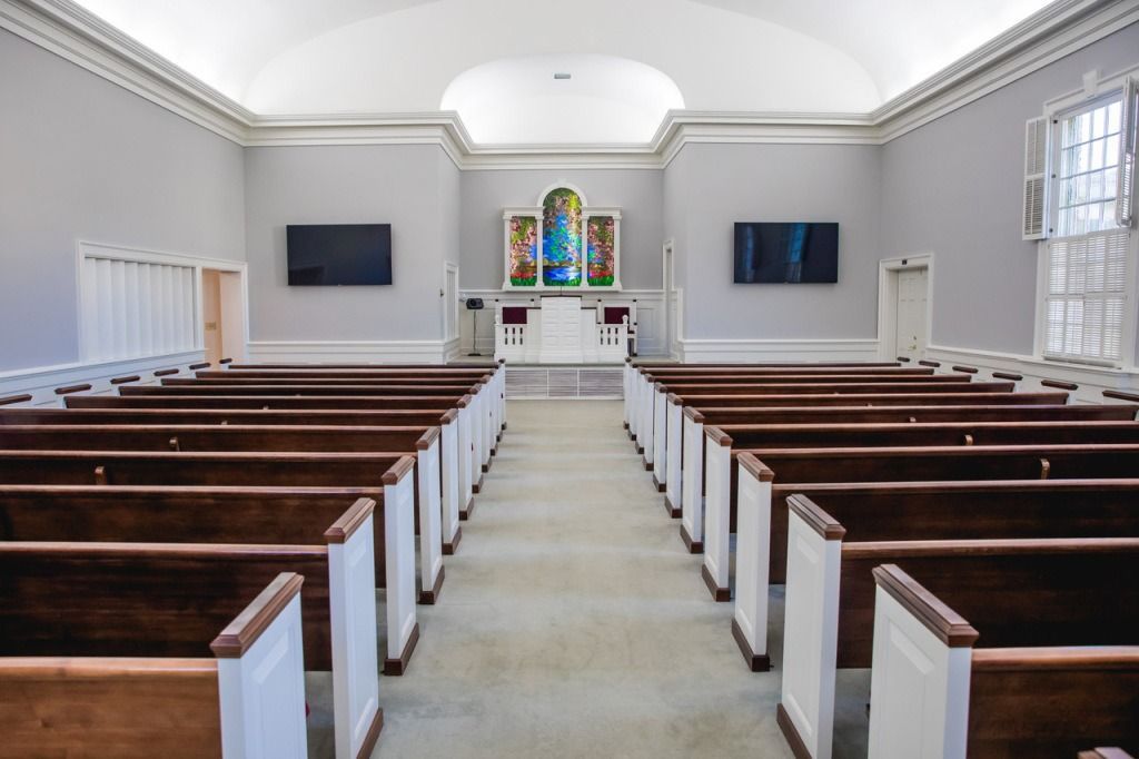 Rows of wooden pews face an altar with stained glass in a light-filled chapel.