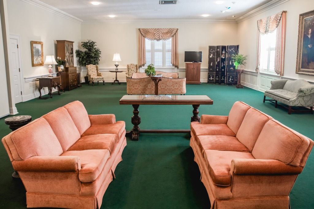 Room with two peach-colored sofas, dark green carpet, light walls, and various furniture.