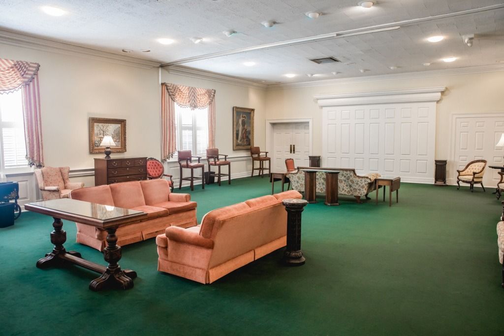 Spacious room with green carpet, several couches, chairs, and tables. Soft pink and beige colors.