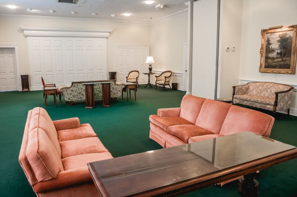 Lounge with coral sofas, green carpet, and a painting; neutral setting suggests a waiting or gathering space.