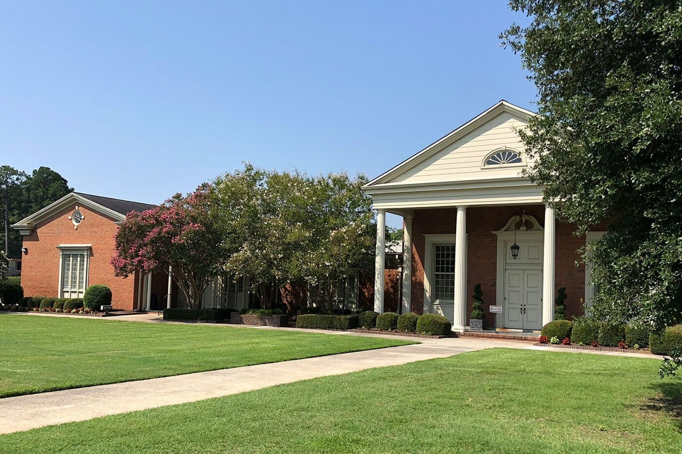 Two brick buildings with white accents, set in a green lawn under a blue sky.