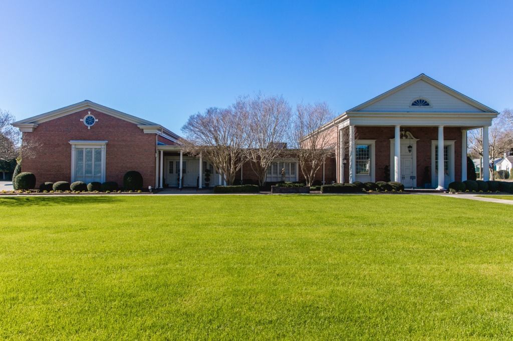 Red brick building with white columns and a green lawn under a clear blue sky.