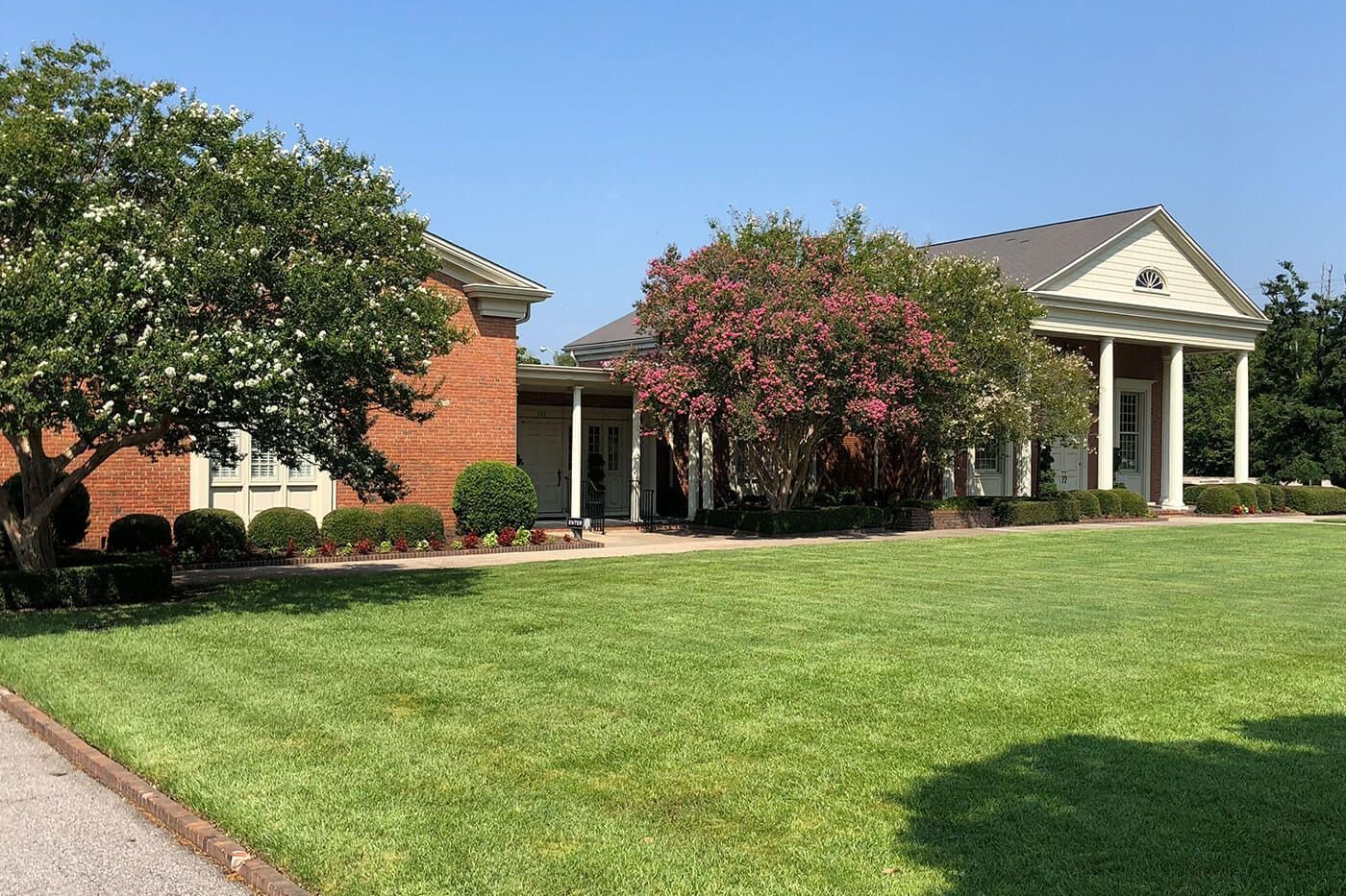 A brick building with white columns and a green lawn under a clear blue sky.