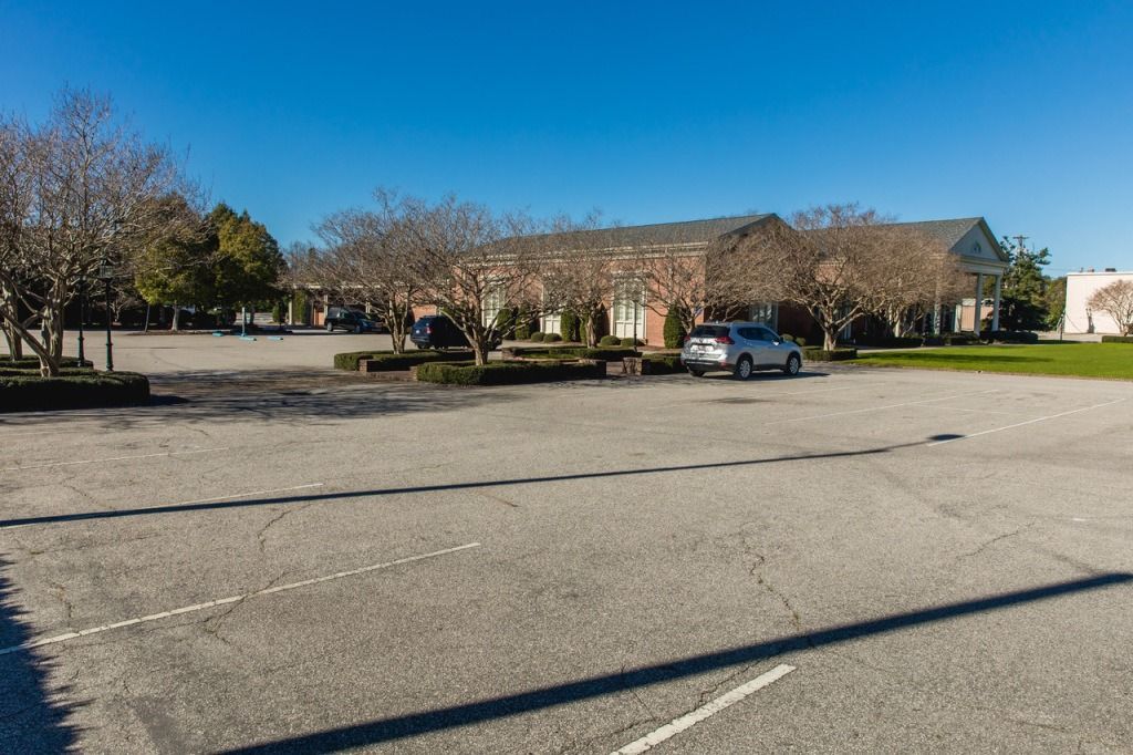 Empty parking lot in front of a low, light-colored building under a clear blue sky.