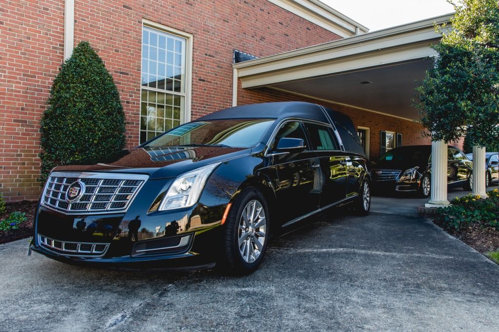 Black hearse parked under a covered entrance of a brick building.