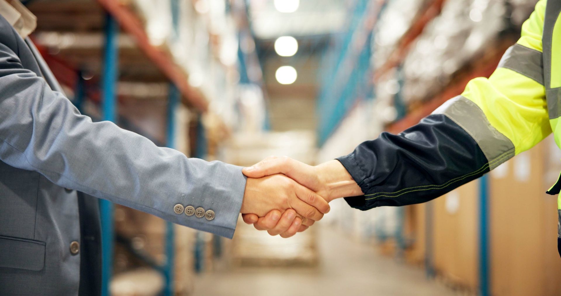 Close-up of a business professional and warehouse worker shaking hands in a warehouse.