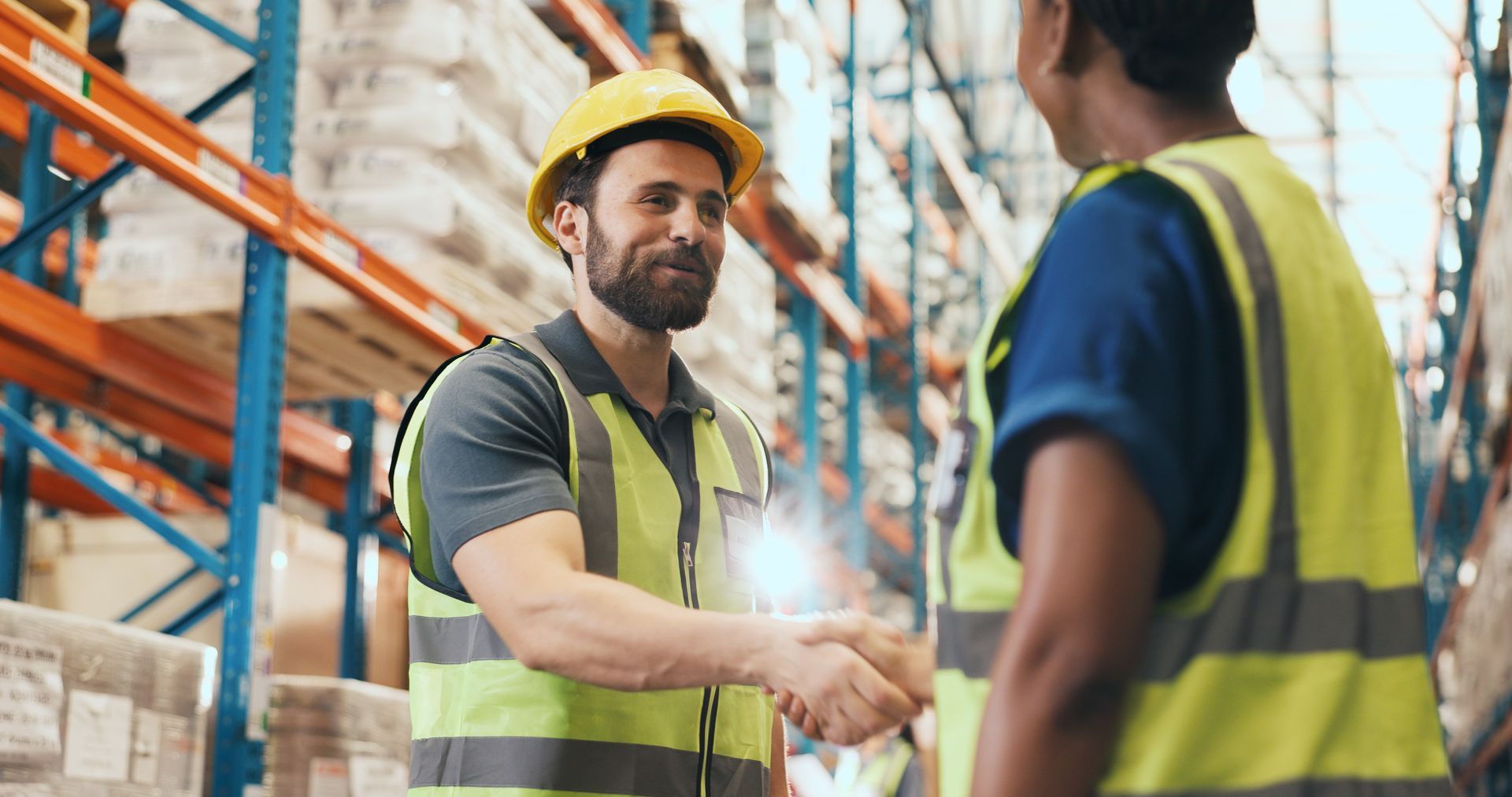 Warehouse workers in safety vests and hard hats shaking hands in an aisle. Warehouse workers in safety vests and hard hats shaking hands in an aisle.