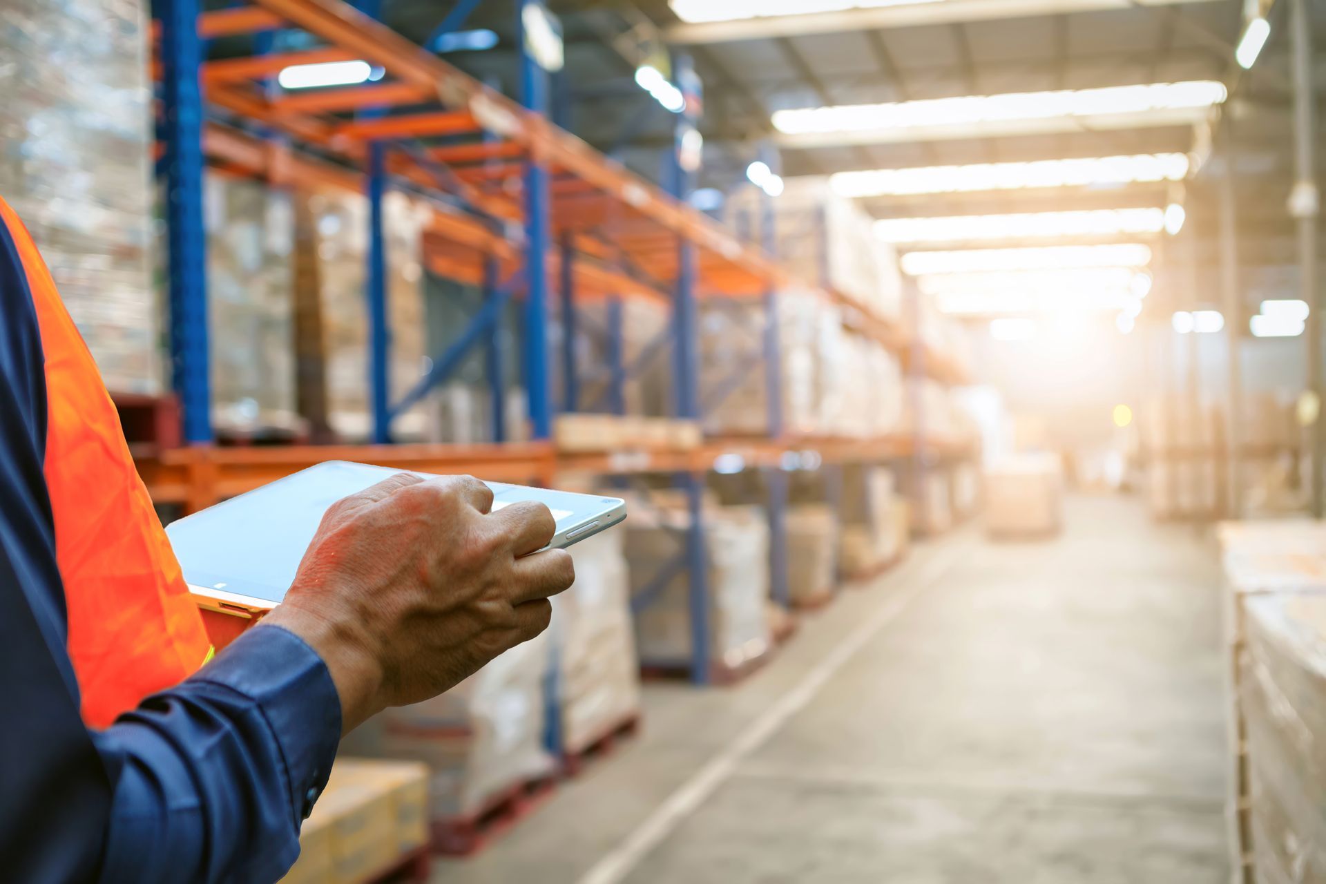 Worker using a tablet to manage inventory while standing in a large warehouse aisle. Worker using a tablet to manage inventory while standing in a large warehouse aisle.