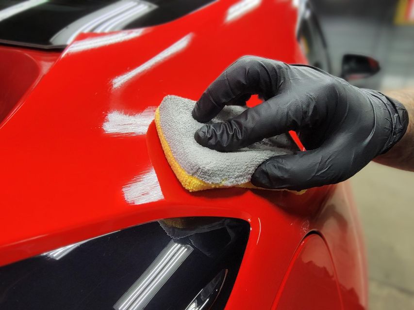 A person wearing black gloves is cleaning a red car with a sponge.