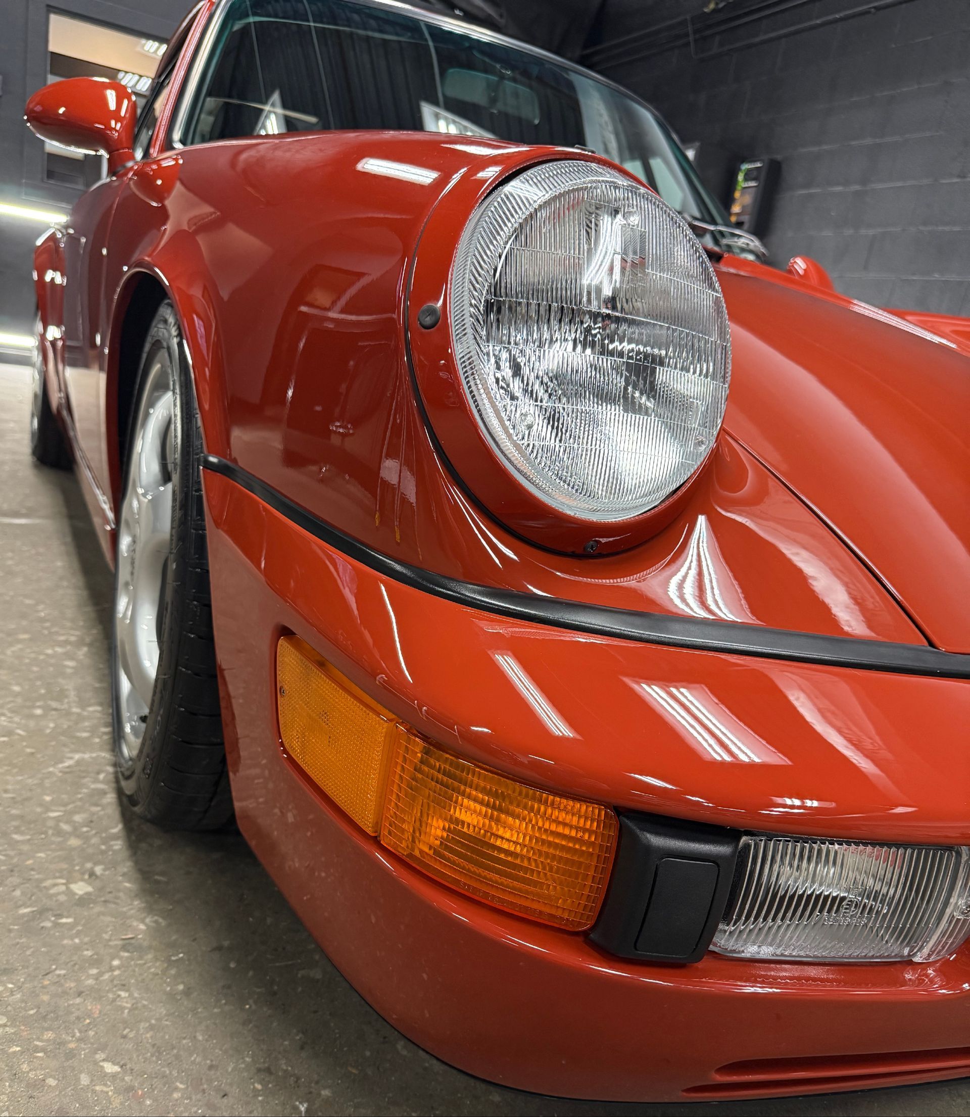 Close-up of a red classic sports car’s front headlight and bumper indoors