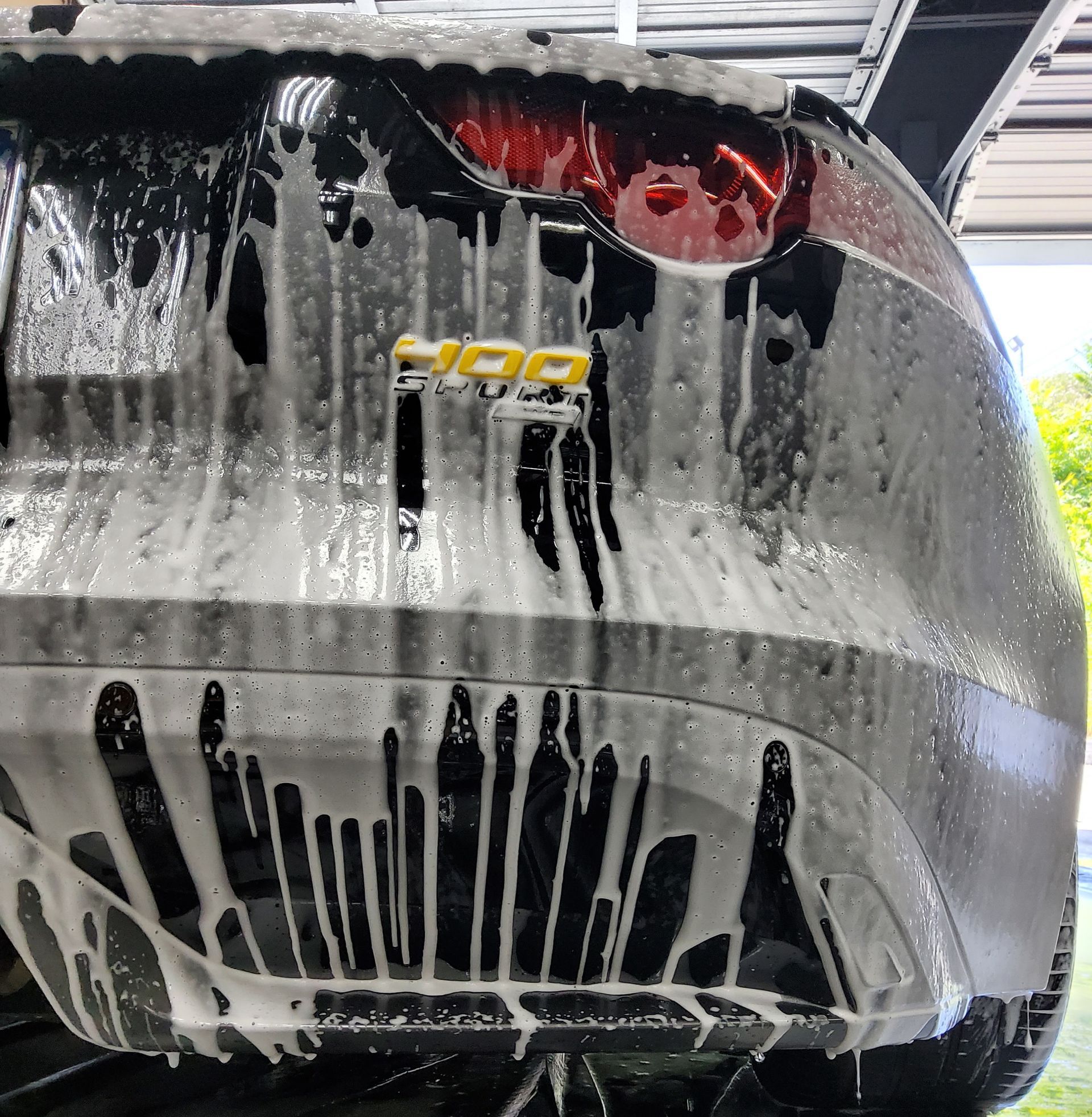 A man is cleaning the wheel of a black car with a sponge.
