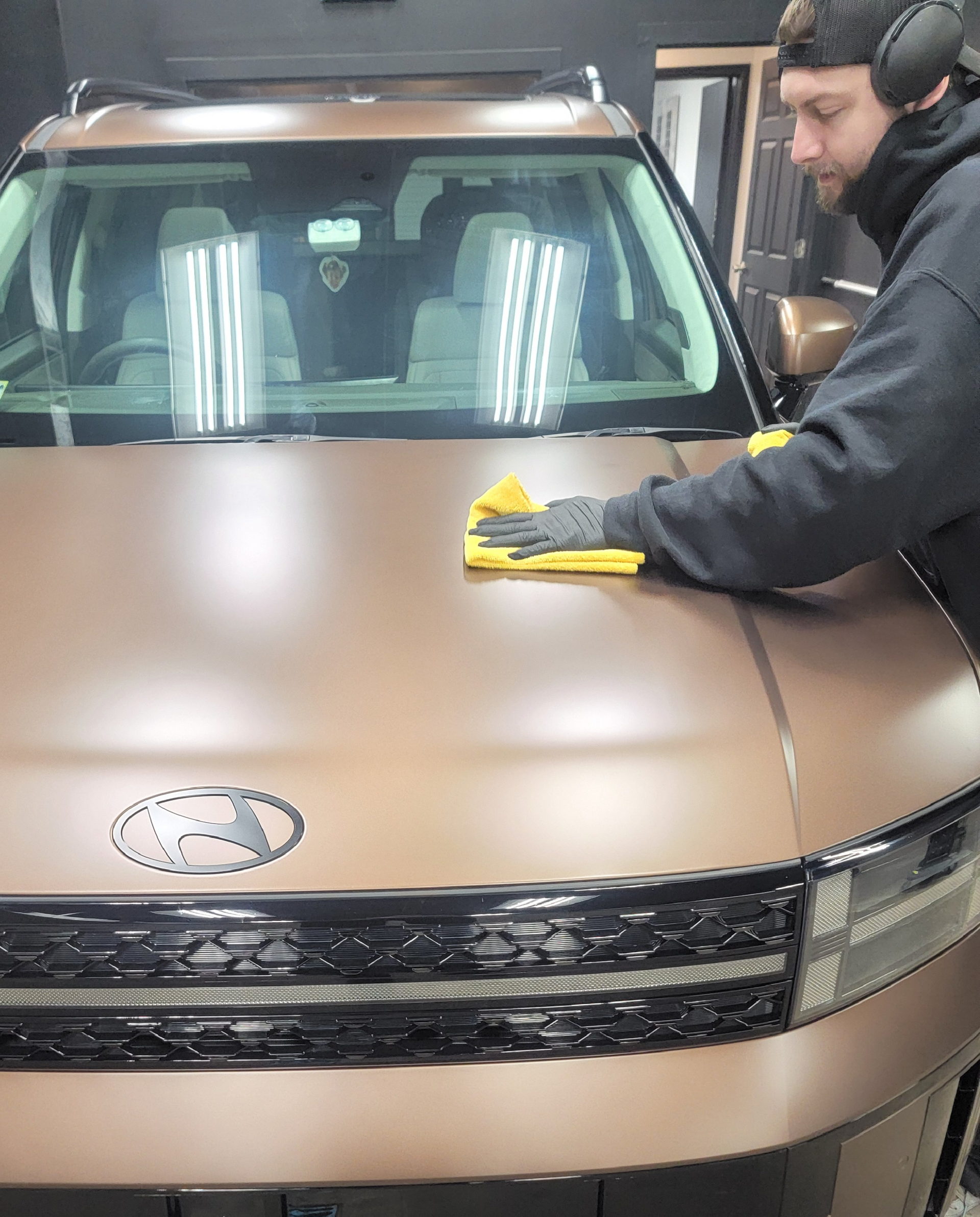 Person wiping a bronze car hood with a yellow cloth in a garage