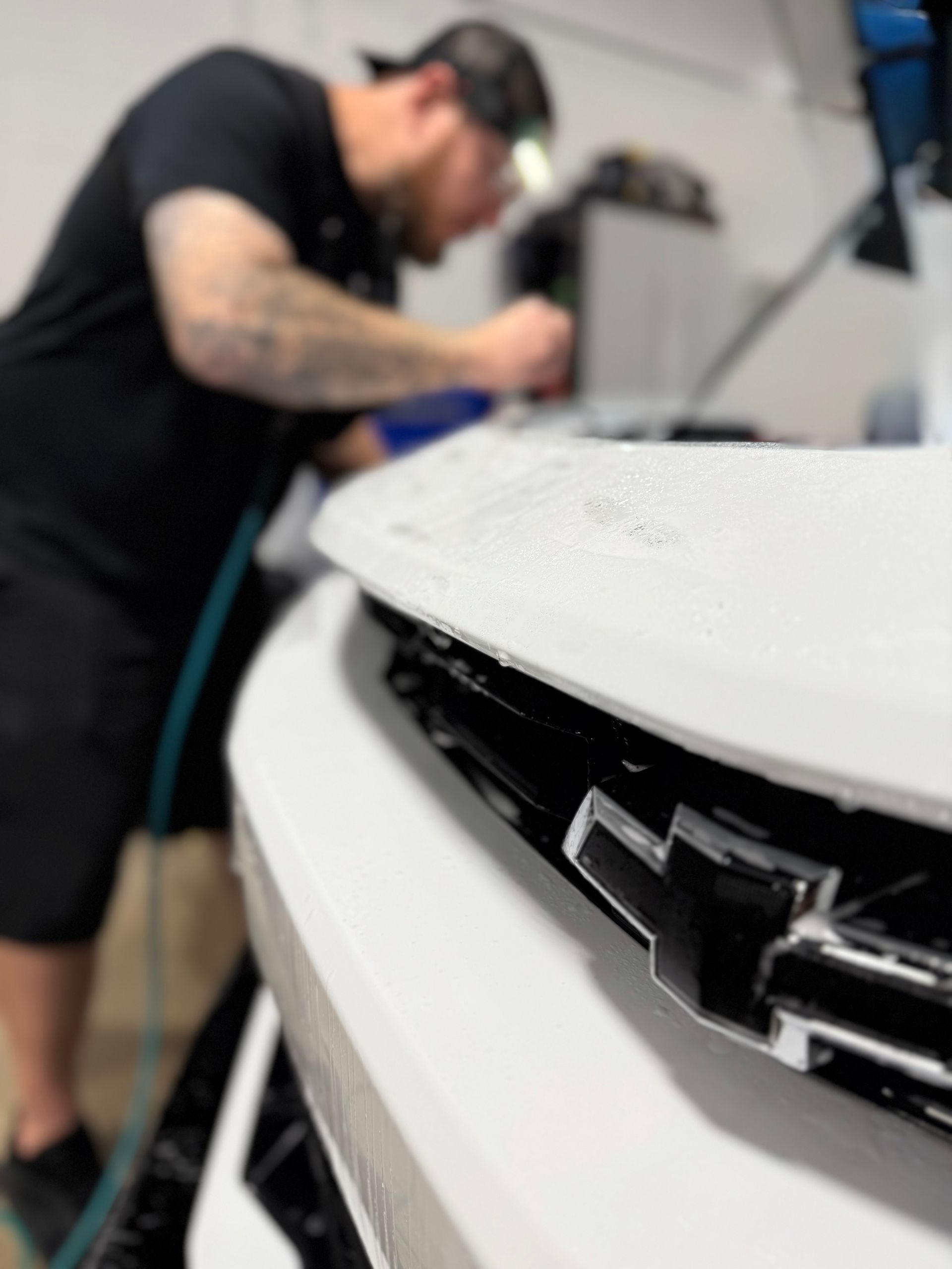 A man is applying a protective film to the hood of a red car.