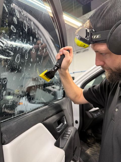 A man with a tattoo on his arm is working on the roof of a car.