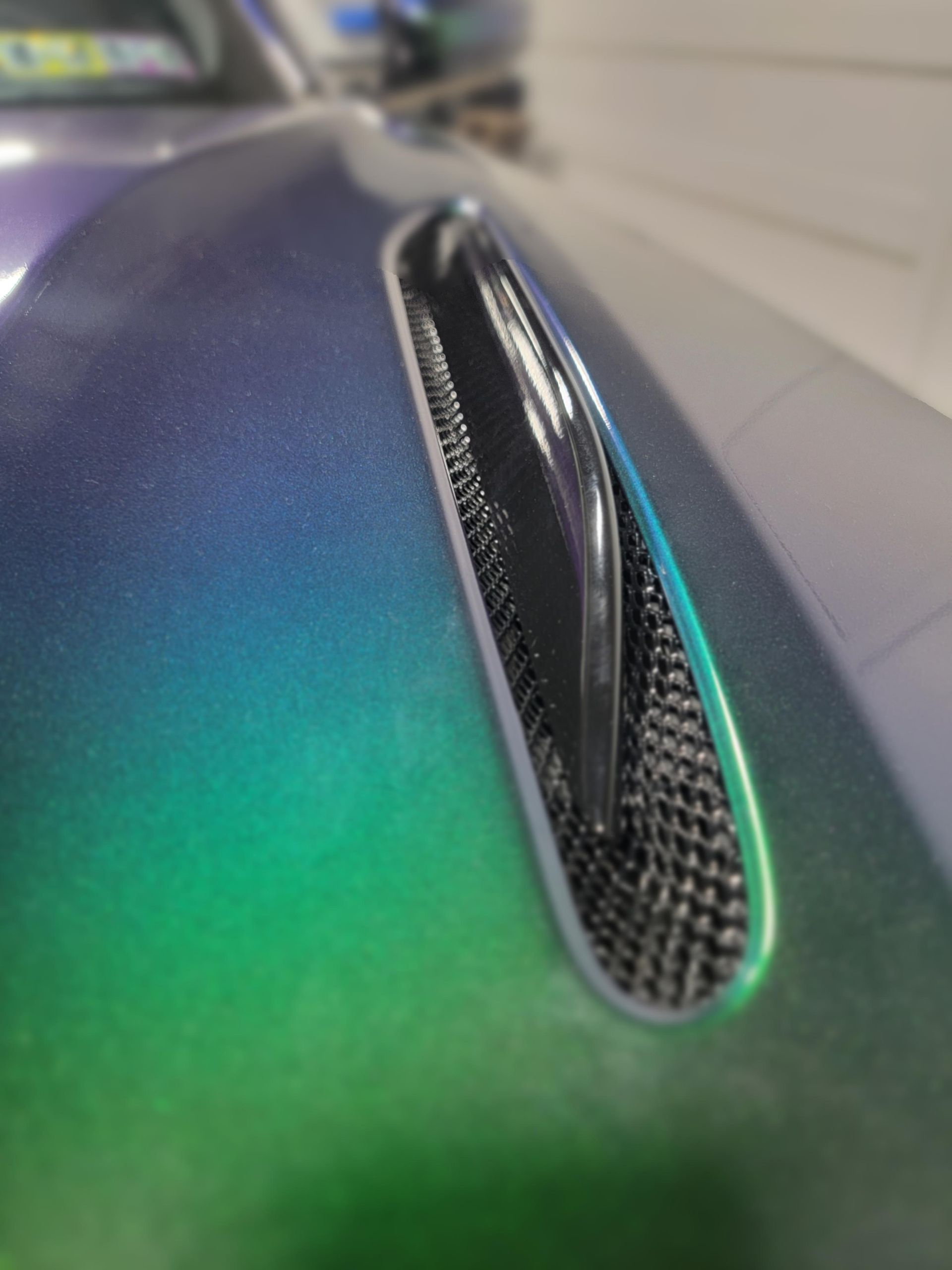 Close-up of a black mouse with a green-blue gradient shell and a carbon-fiber side vent