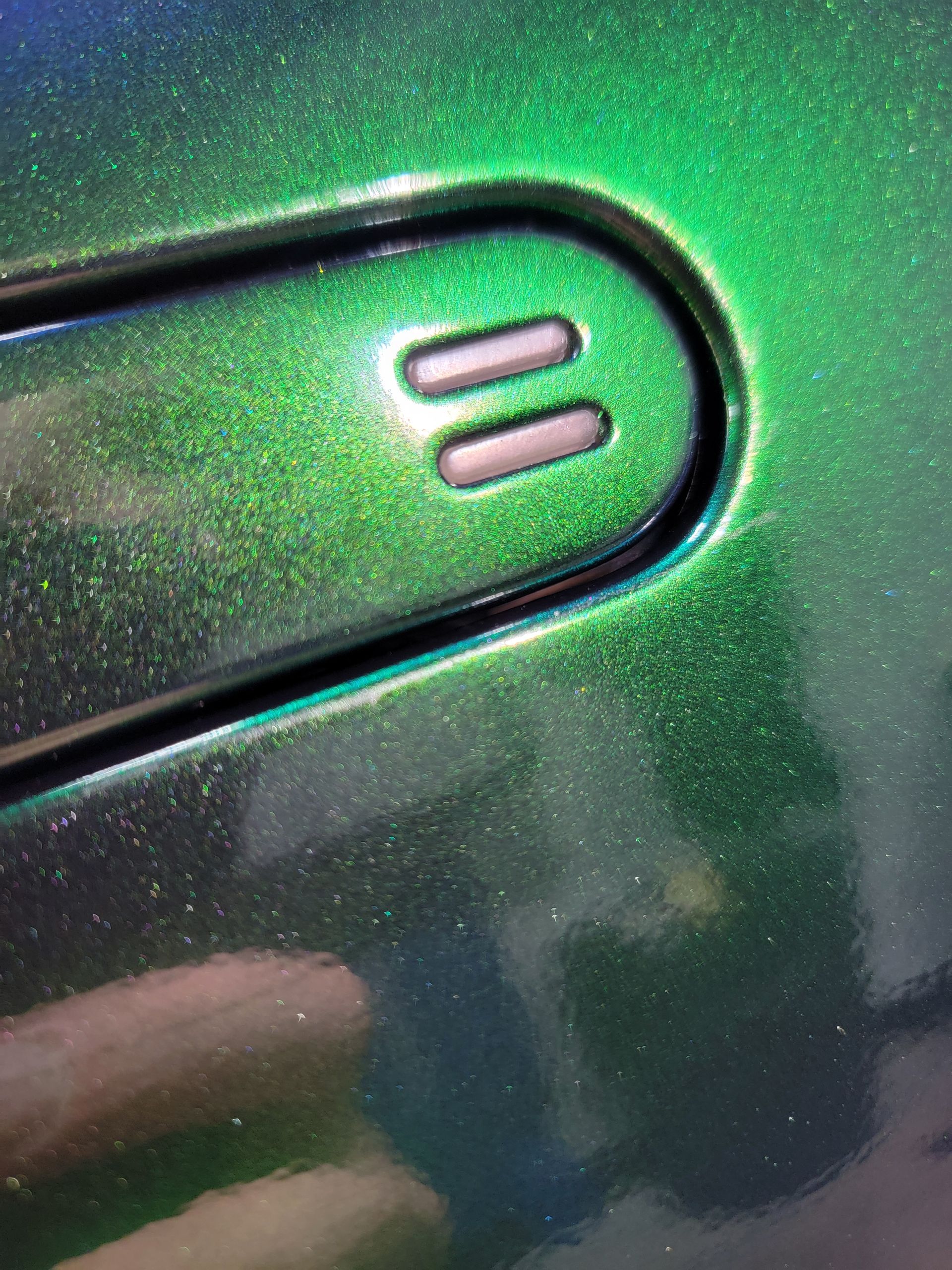 Close-up of a green metallic device with two small oval buttons outlined in pink.