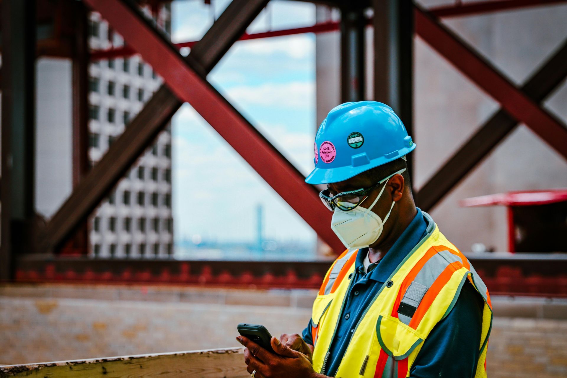 A construction worker wearing a hard hat and mask is looking at his cell phone.