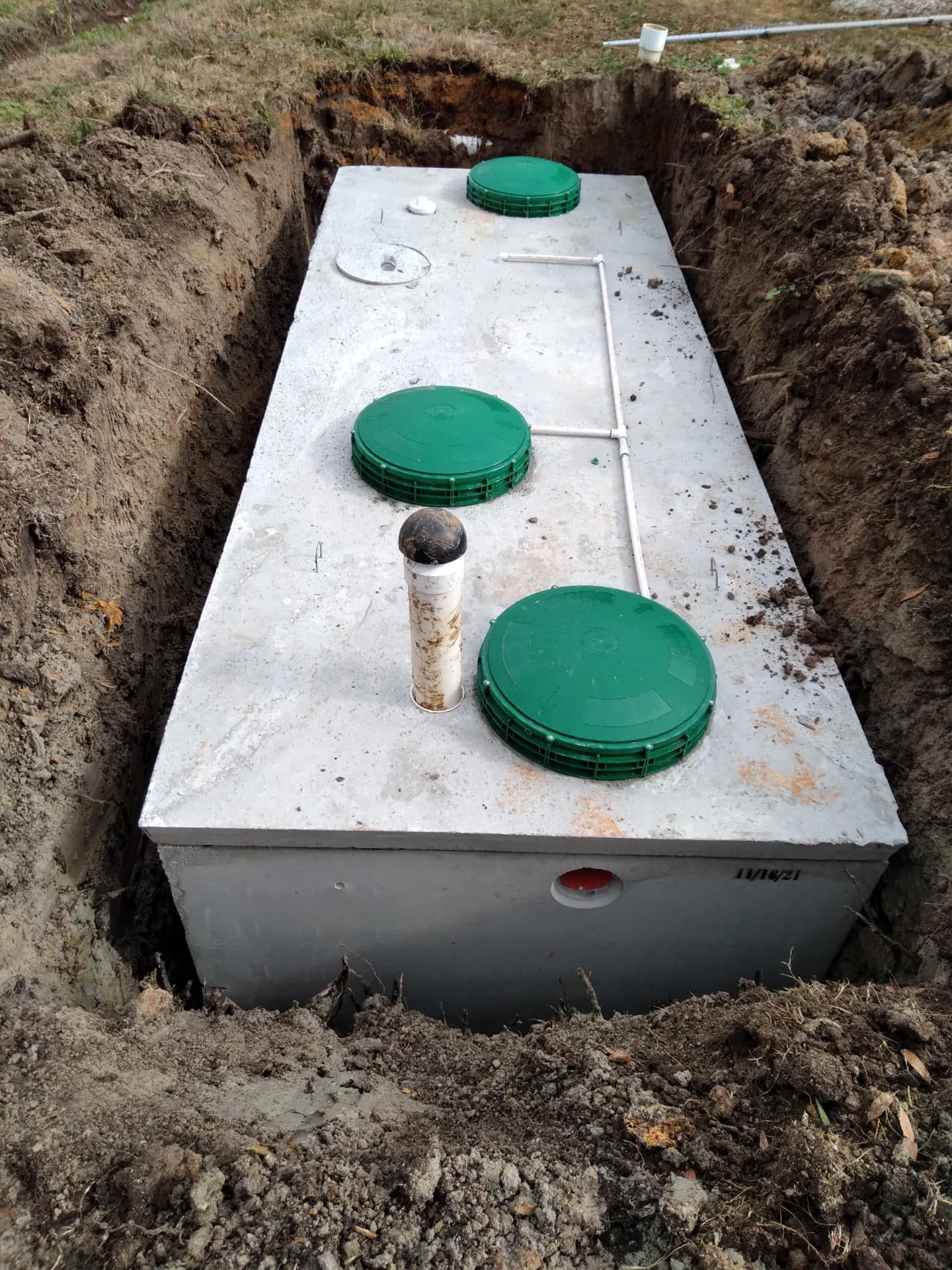 A rectangular concrete septic tank, green access lids, installed in an excavated trench.