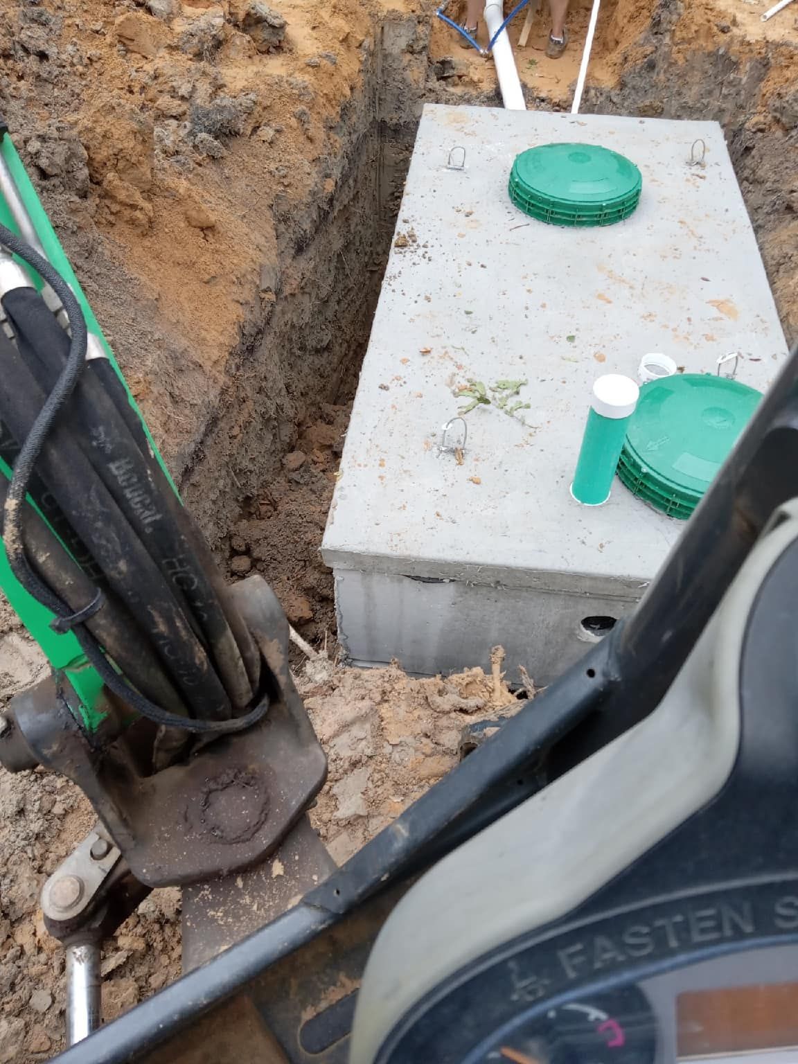 Septic tank being installed in a trench; green lids, dirt, and equipment visible.