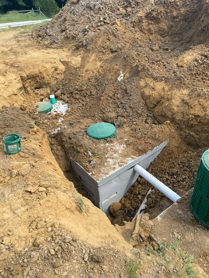 Excavated septic system components in a dirt trench, including a tank, pipes, and lids.