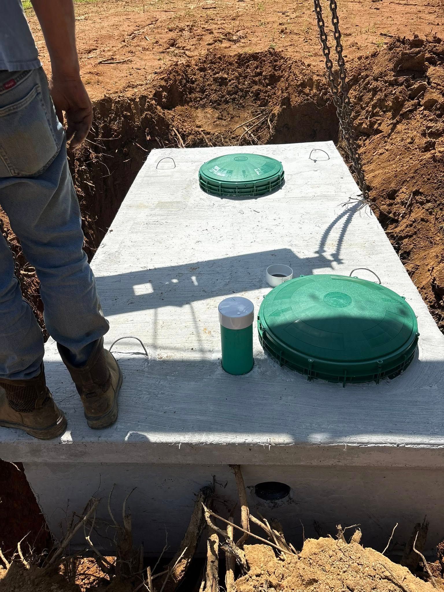Concrete septic tank being installed in a dirt trench, with a person standing nearby.