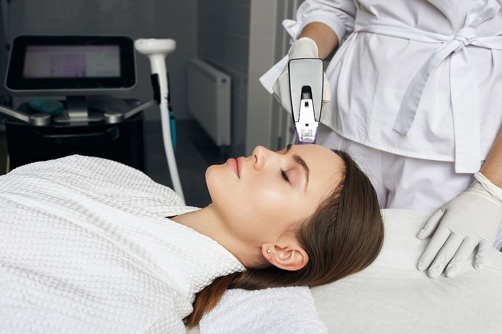 Woman receiving Morpheus8 facial laser treatment in a medical office; technician in white coat.
