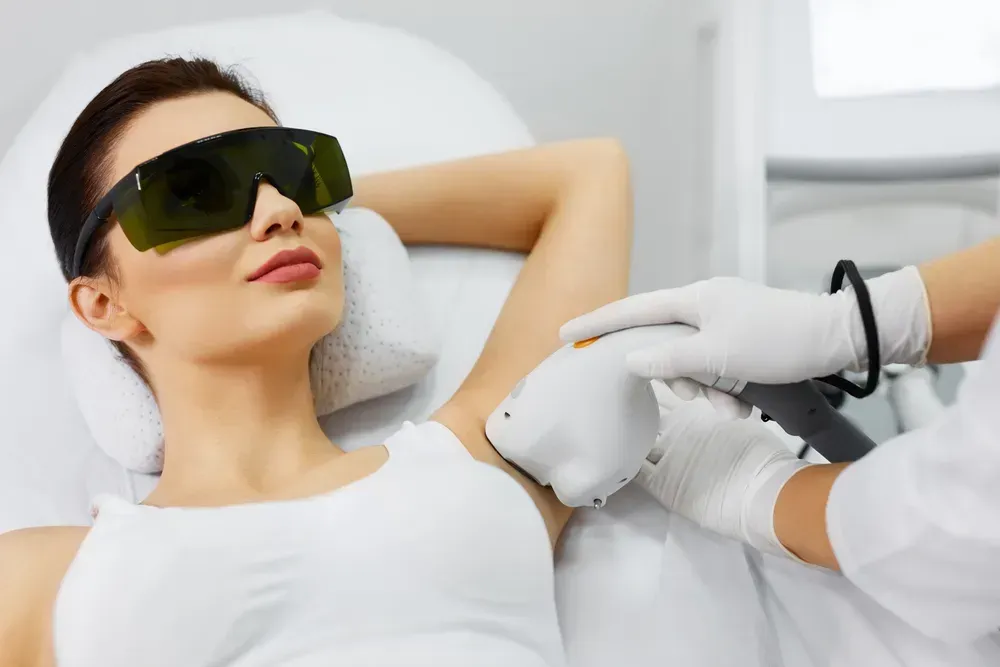 soprano-ice-laser-hair-removal Woman receiving laser hair removal on her armpit while wearing protective eyewear. The medical setting is a spa or clinic.