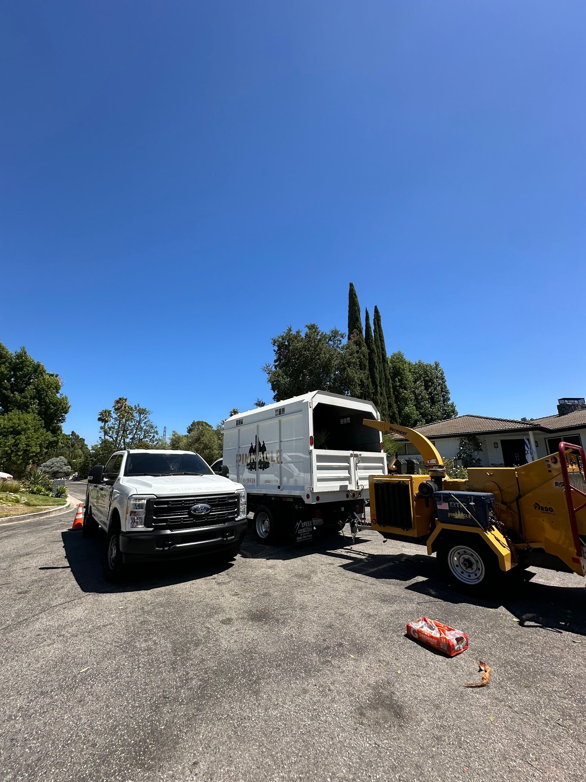 White truck, RV, and yellow loader parked on gravel under a clear blue sky.