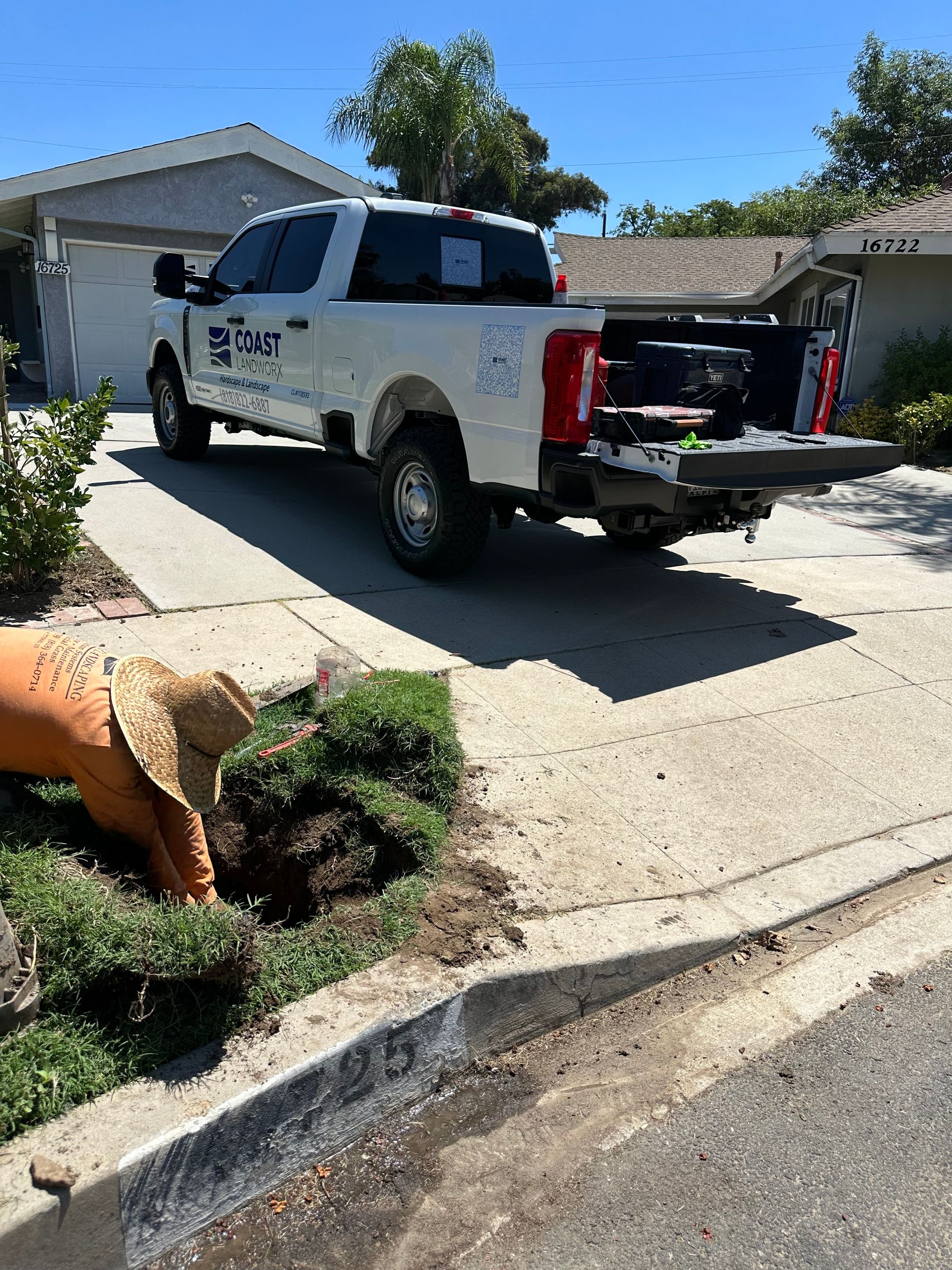 White pickup truck parked in a driveway beside a person digging in a front yard garden.