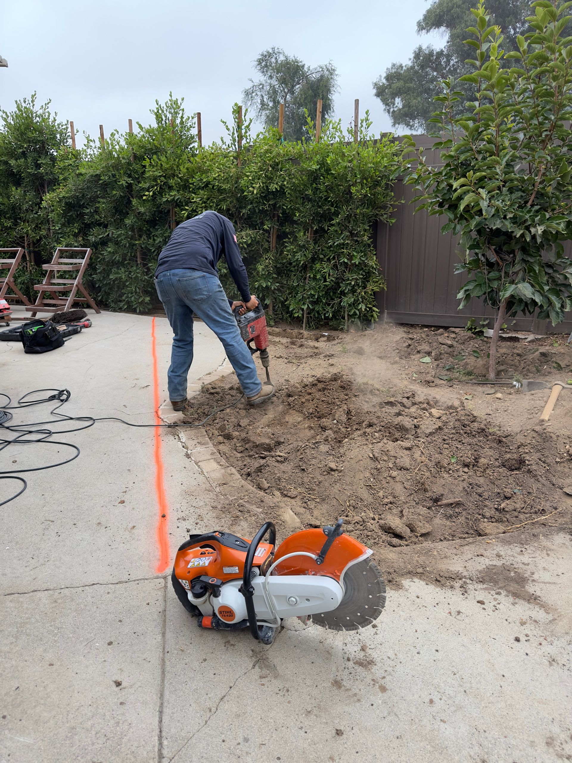 Worker using a chainsaw to cut a concrete slab in a backyard driveway