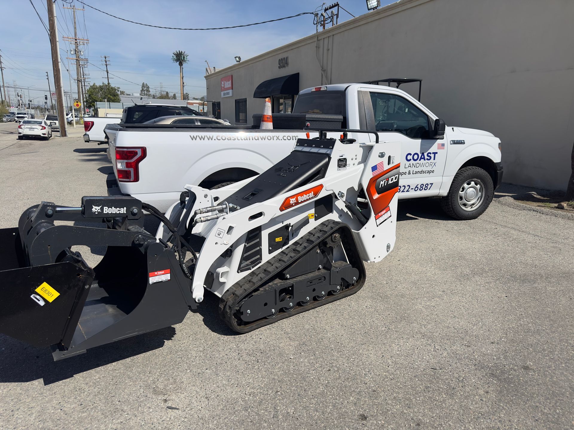 White-and-black skid steer loader parked beside a white pickup truck in an industrial lot.