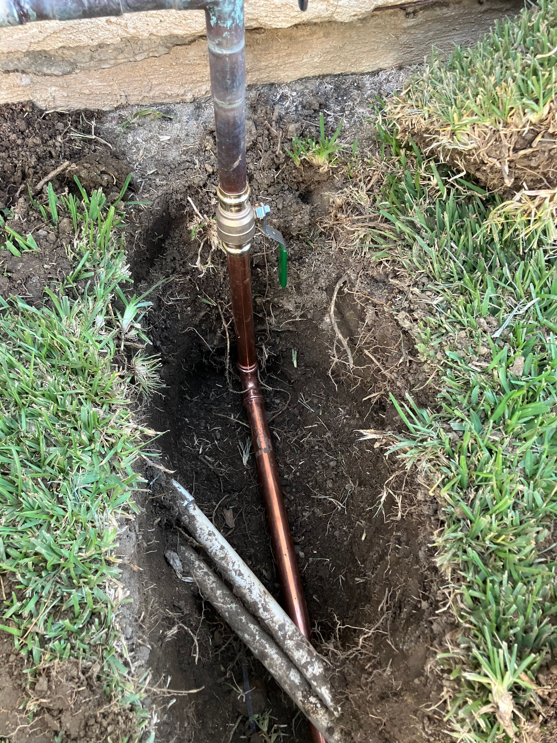 Copper pipe in a dug hole beside a lawn, showing an exposed underground water line repair.