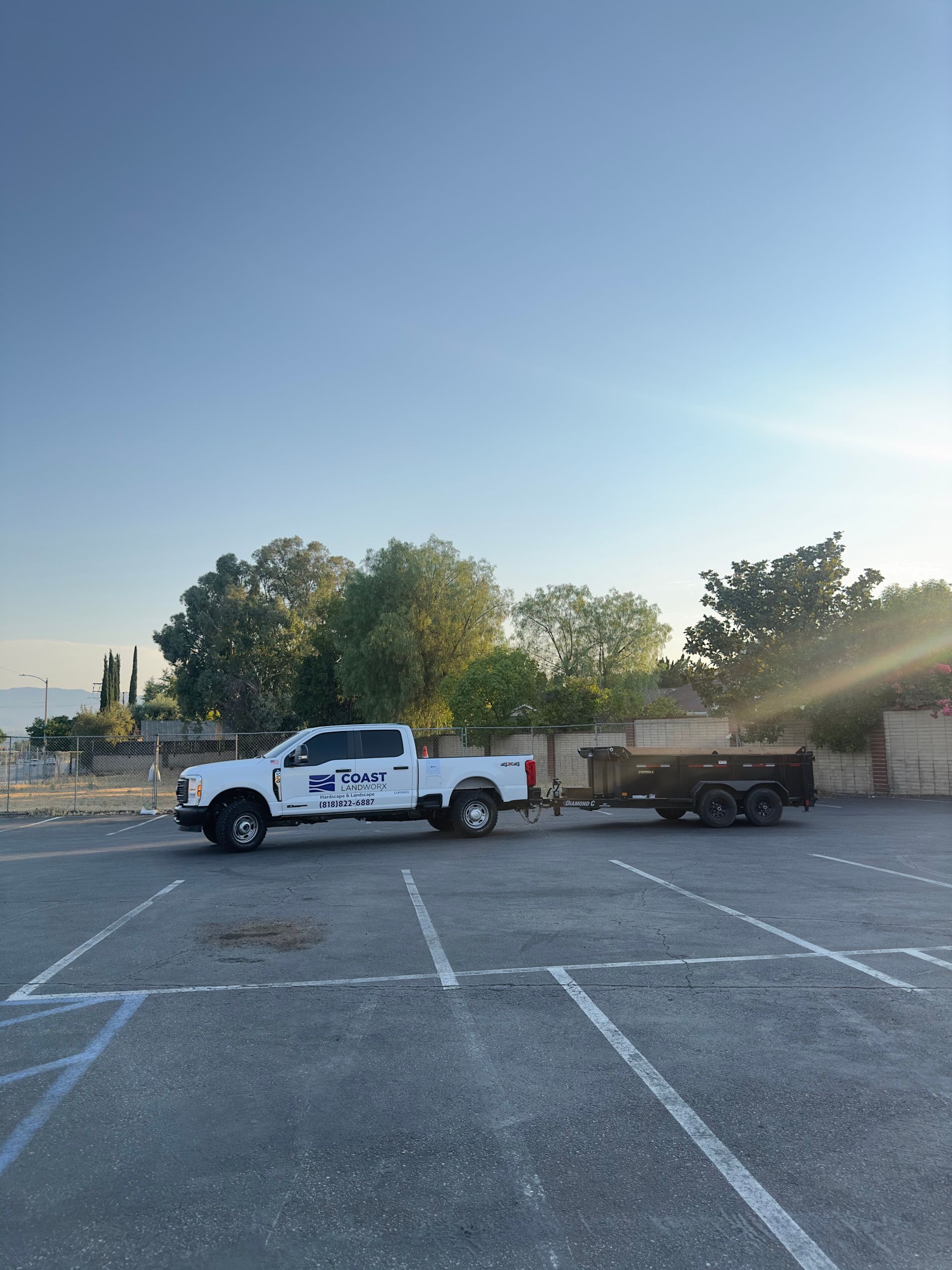 White utility truck towing a flatbed trailer in an empty parking lot at sunset