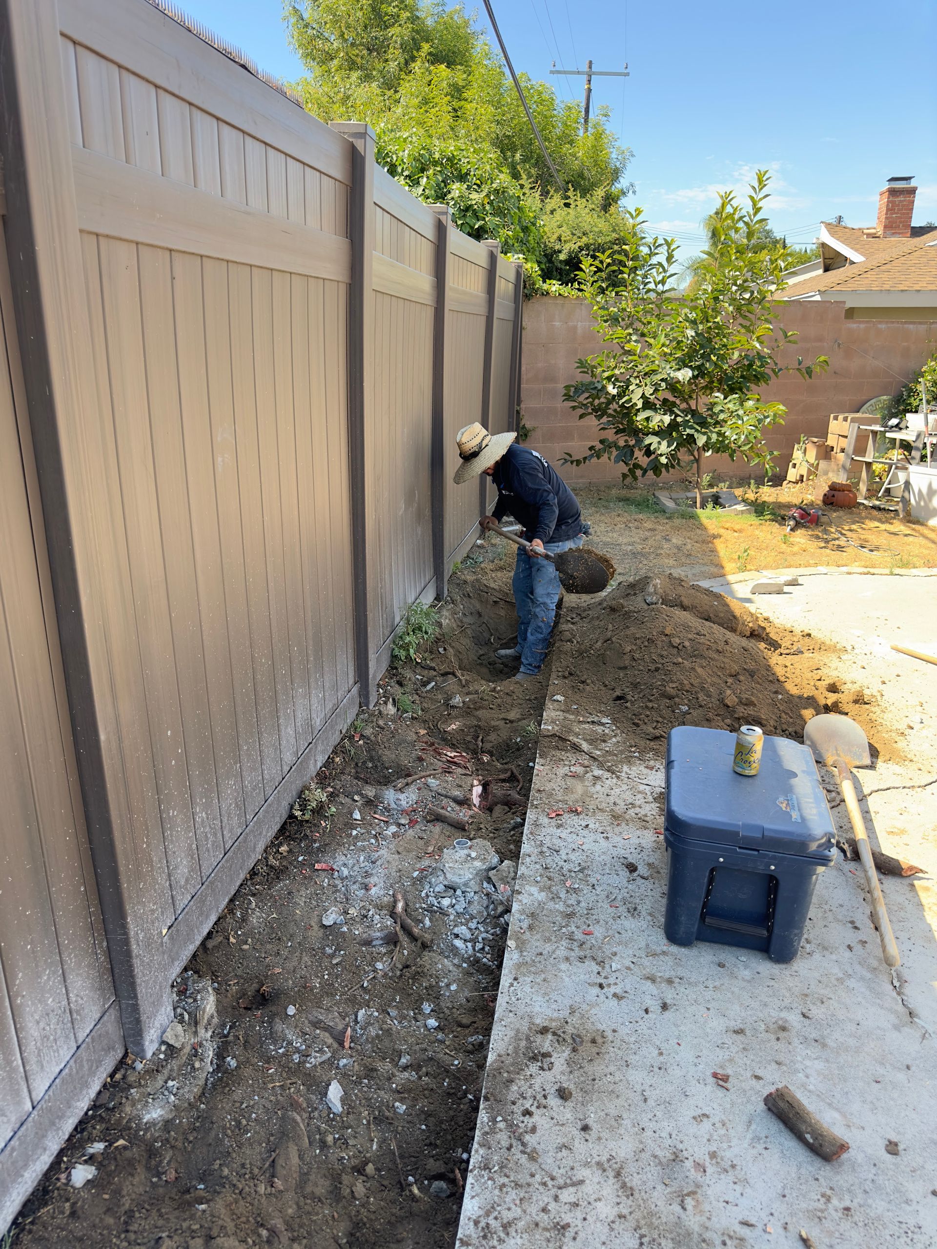 Worker installing a fence along a gravel side yard beside a concrete driveway on a sunny day