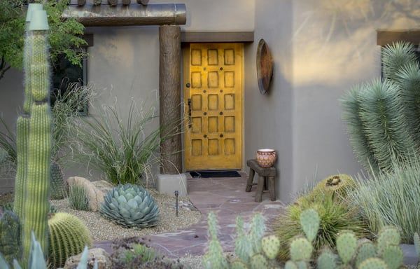 Desert courtyard with cacti and succulents framing a bright yellow door and stucco wall