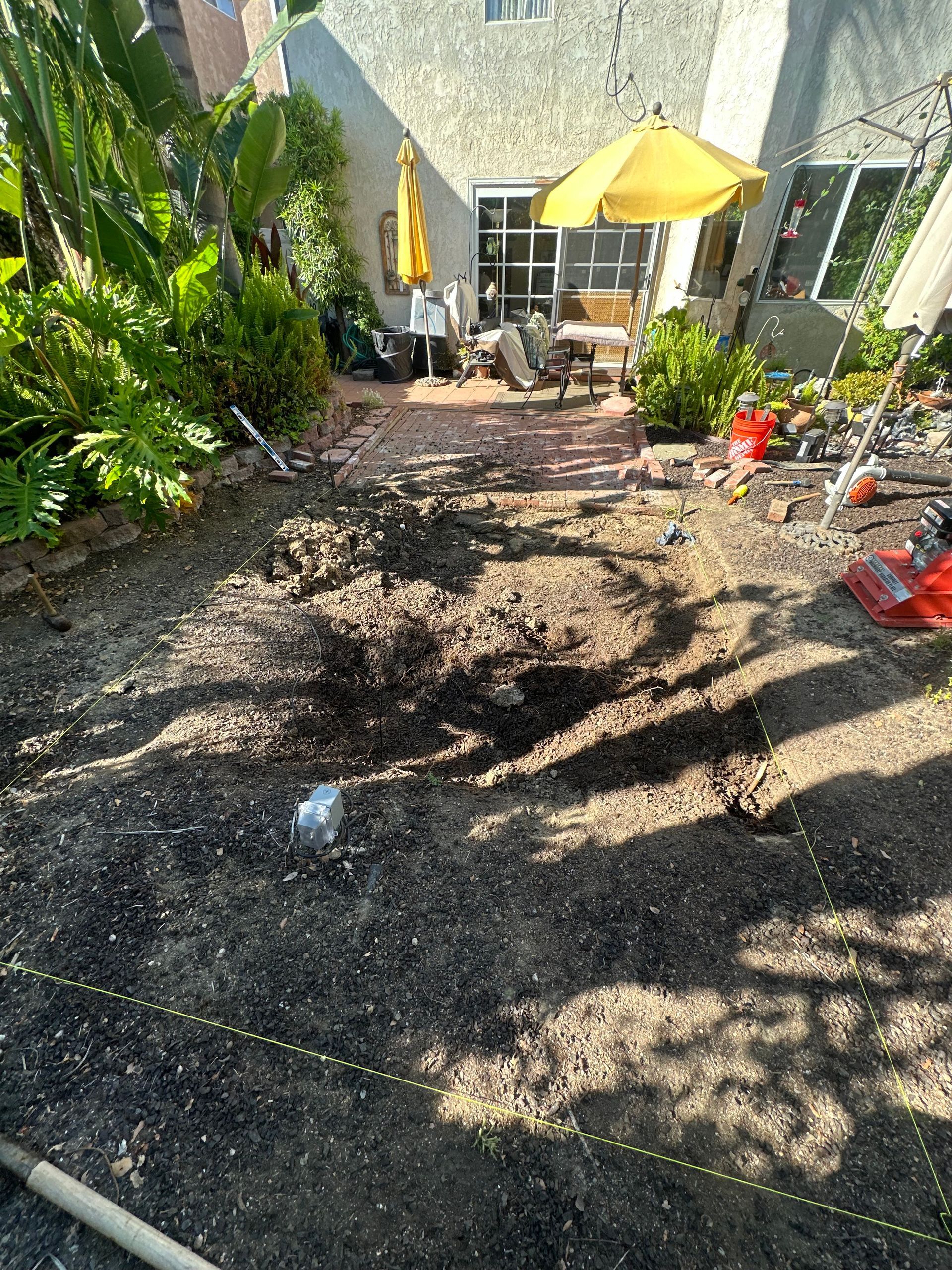 Backyard patio with gravel ground, potted plants, and two yellow umbrellas by a house.