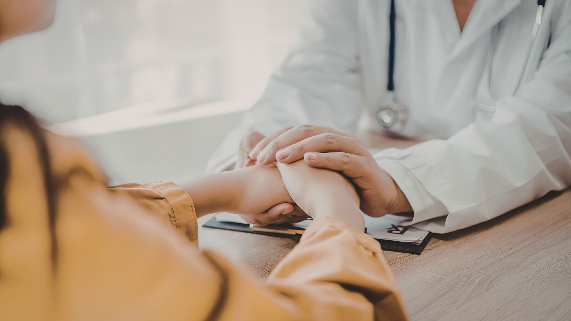 Doctor holding a patient’s hands in a comforting gesture during a medical visit