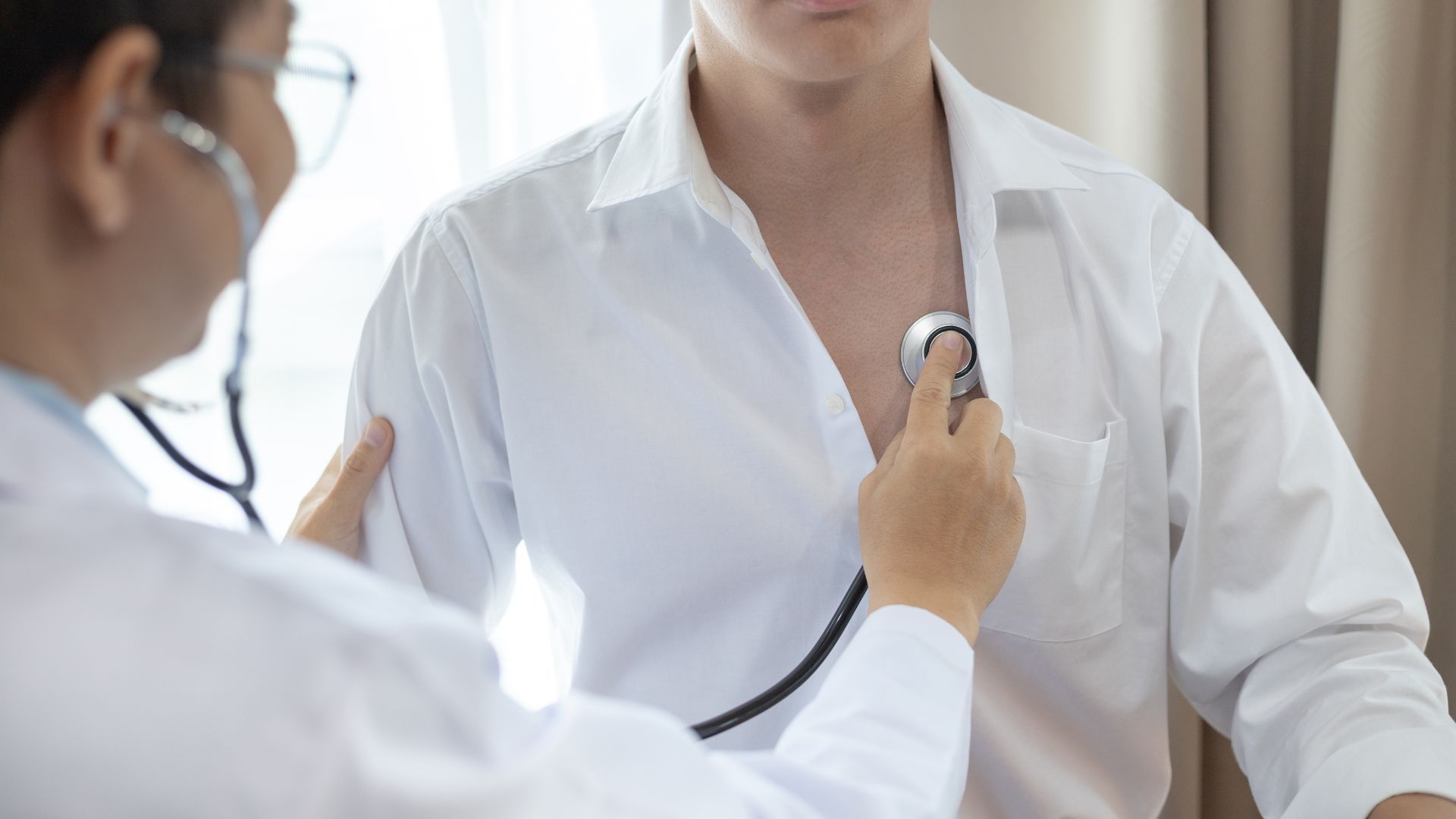Doctor using a stethoscope to examine a patient’s chest in a bright clinic