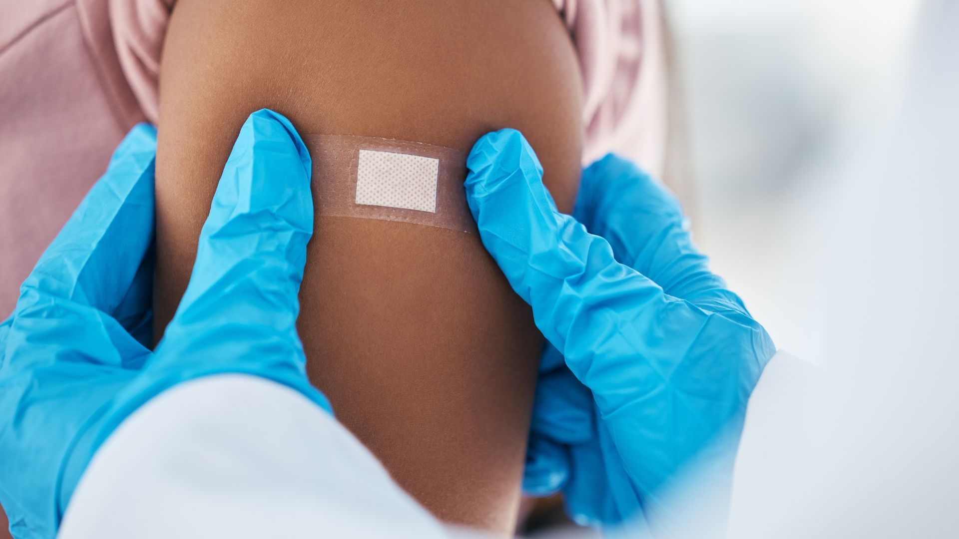 Gloved hands apply a bandage to a child's upper arm after a vaccination