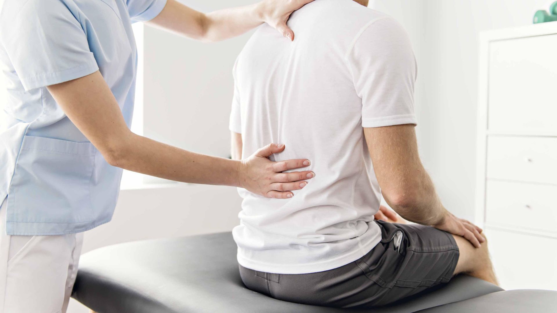 Healthcare worker examining a seated patient’s back in a clinic room
