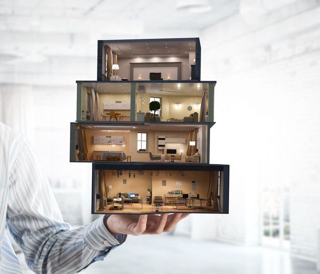 Hand holding a stacked cutaway model of a furnished house interior, with lit rooms visible inside
