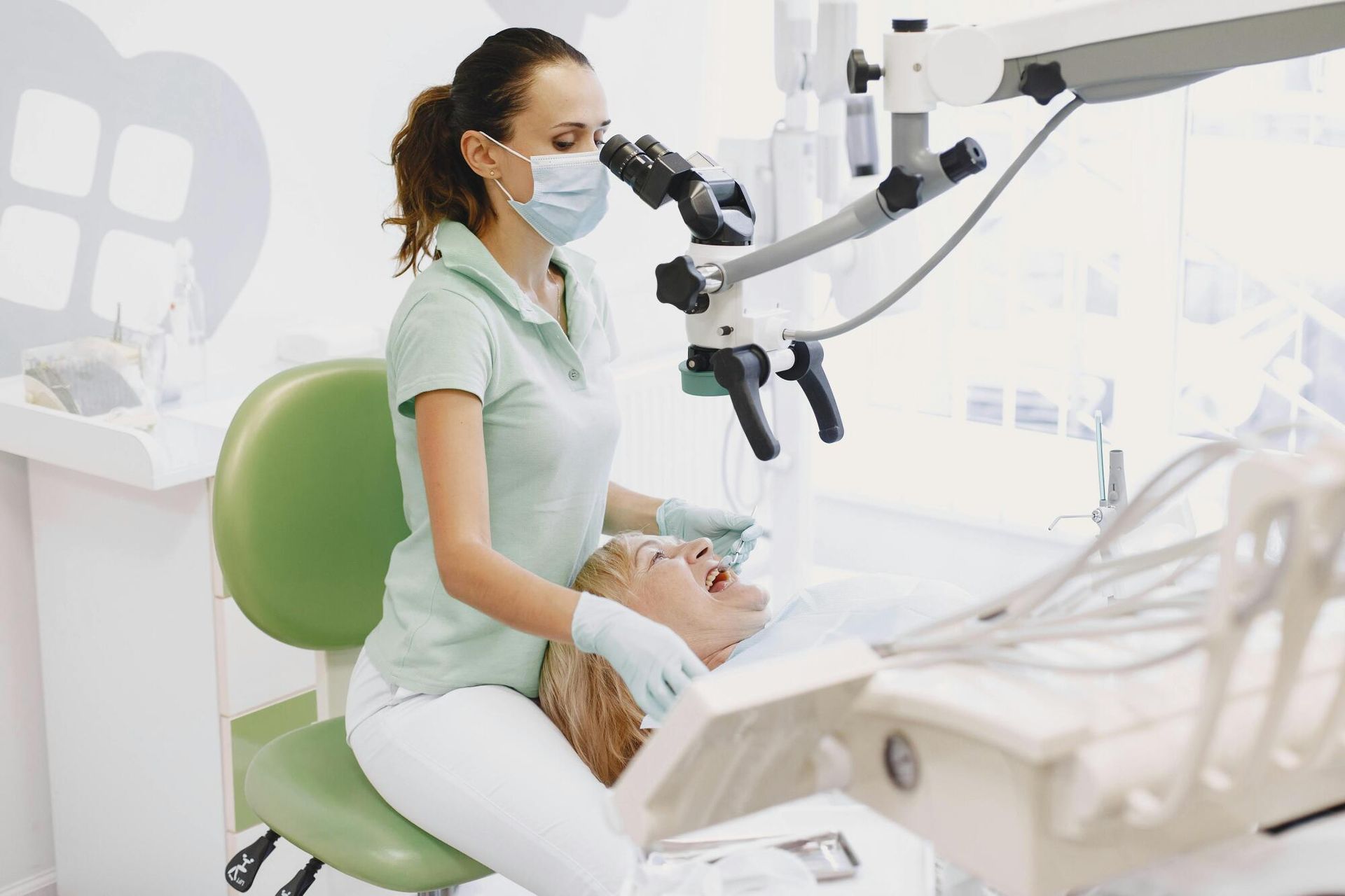 Dentist examining patient's teeth with microscope in a dental office. The patient is in the chair with mouth open.