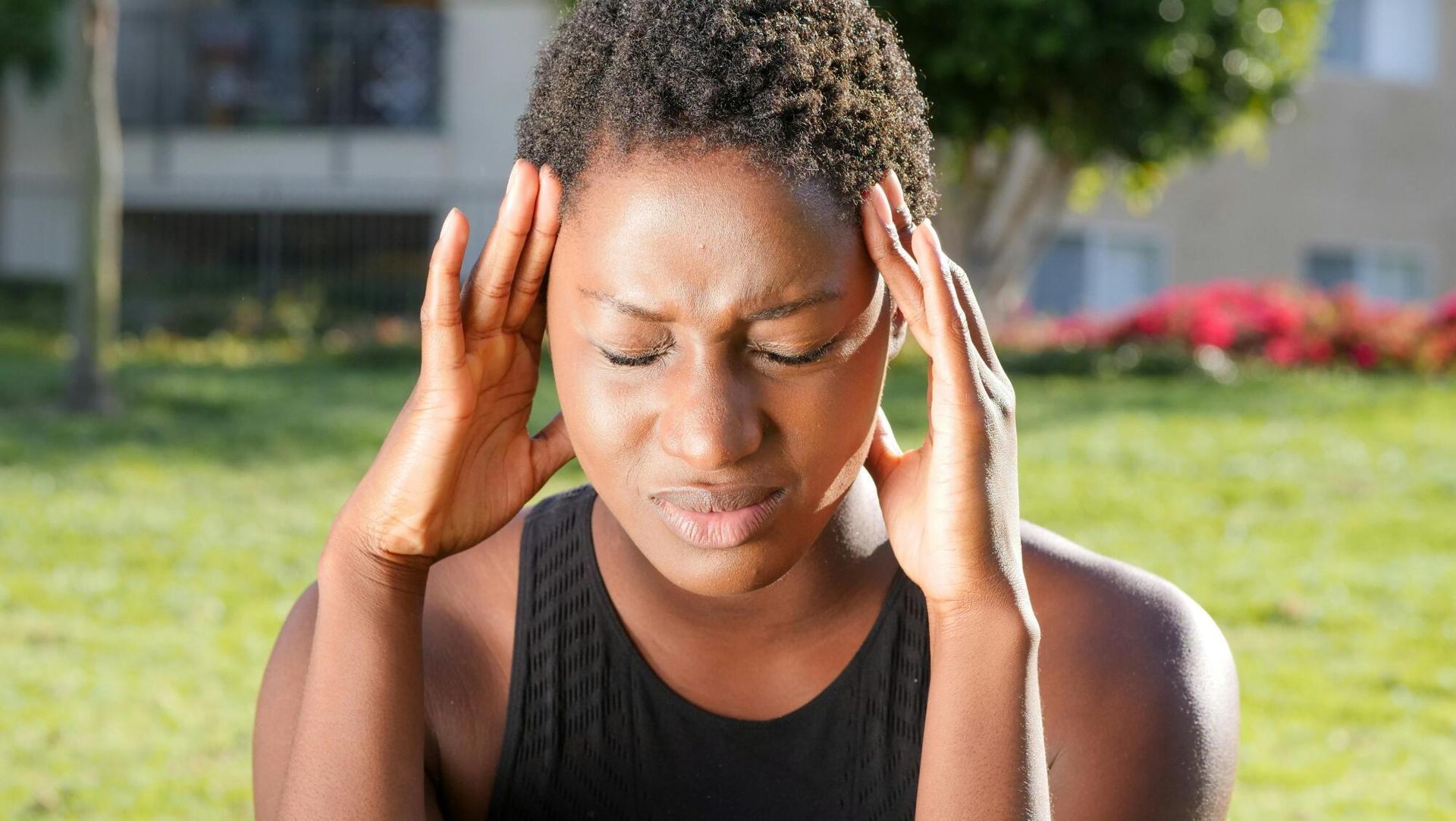 Woman with closed eyes holding temples, appearing distressed outdoors.