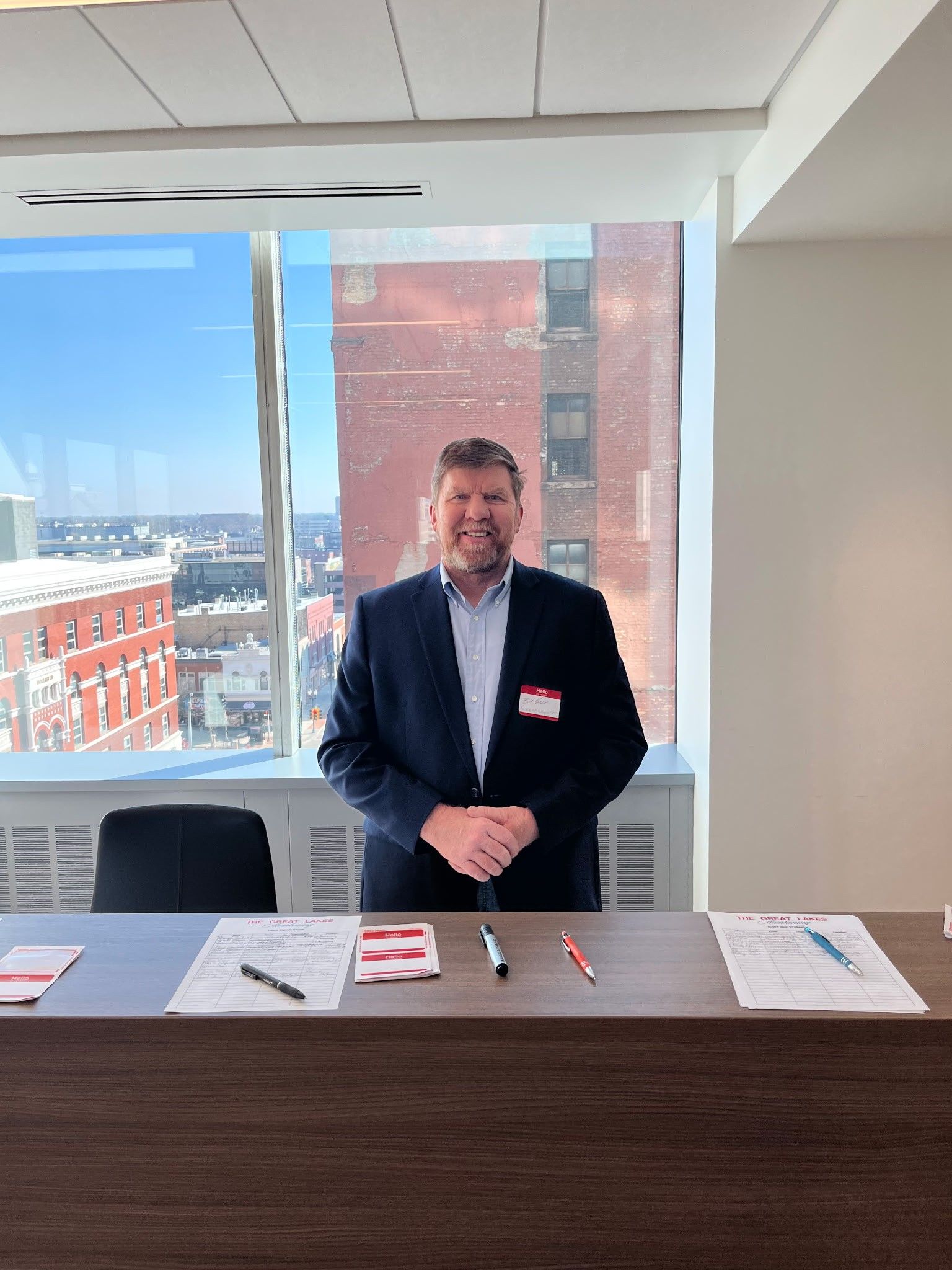Bill kaiser standing behind a table at a windowed conference booth with brochures and pens on display