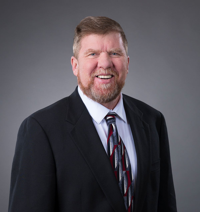 Man in a suit smiles at the camera against a gray background.