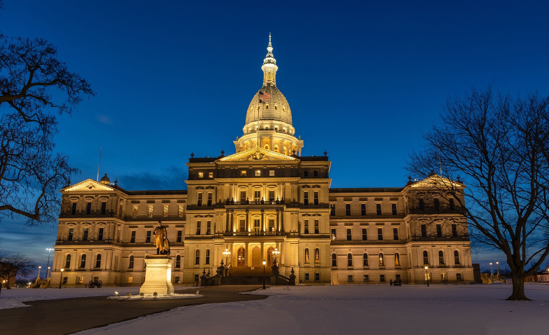 Michigan State Capitol building at dusk, illuminated, snow-covered grounds.