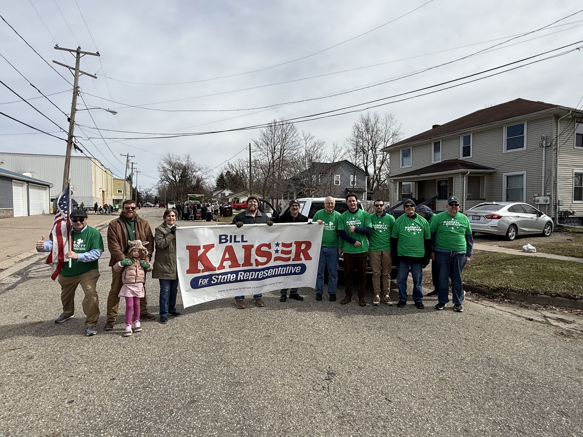 Group of people holding a “Kaiser” campaign banner on a residential street.
